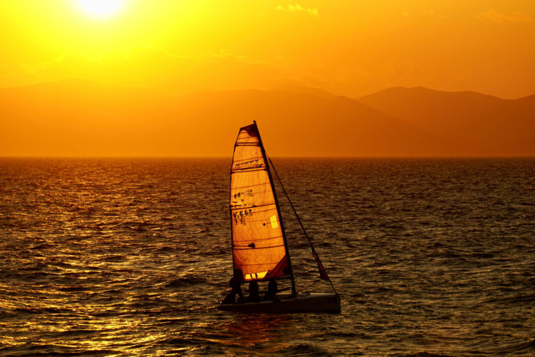 Sailing sailboat on the Sea of Japan at sunset. Orange sunset on the sea and sailing sailboats on it. A sailboat in the sunset in Vladivostok, Russia